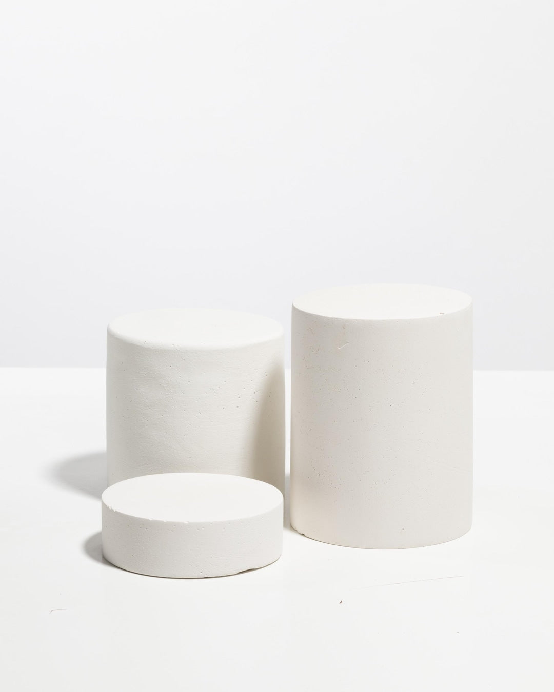 Set of three matte white cylinder display pedestals in varying heights