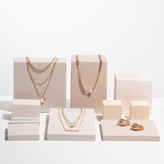 Gold necklaces and rings displayed on off white geometric jewelry display blocks