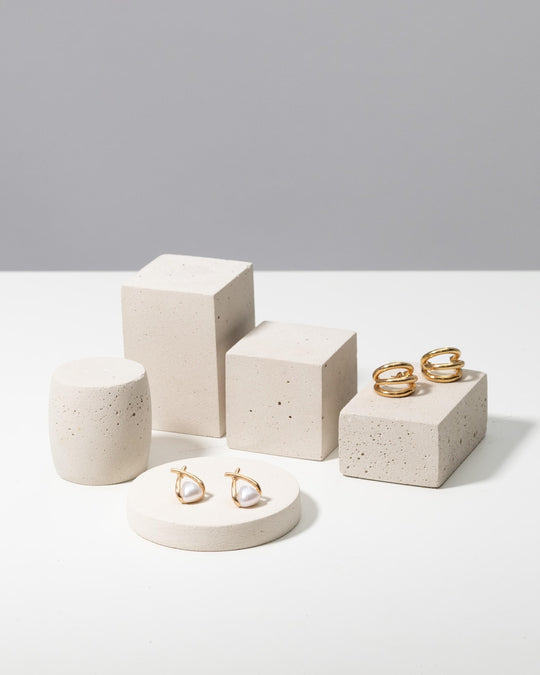 Gold hoop and pearl earrings displayed on off white concrete photo prop pedestals