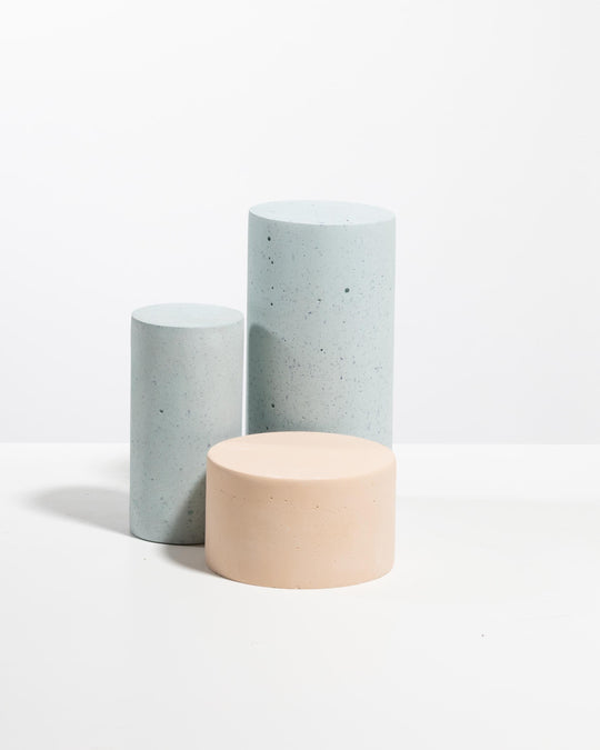 Three cylinder display podiums: two light blue speckled pedestals and one pale peach pedestal