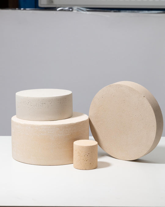 Four round plaster pedestals in beige and off white stacked for styling