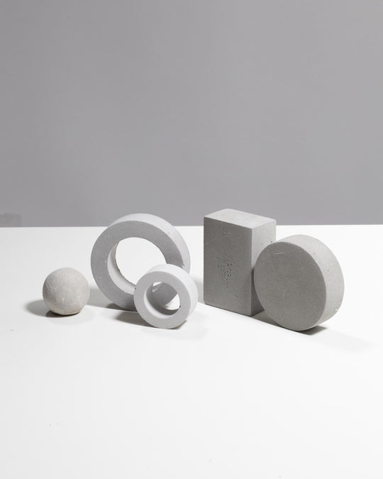 Five geometric plaster shapes in light grey arranged for styling