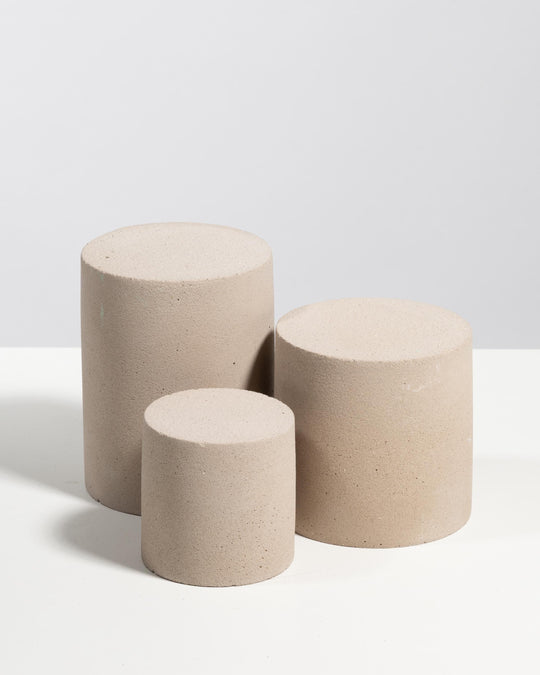 Three light beige plaster cylinder pedestals in tiered heights for display