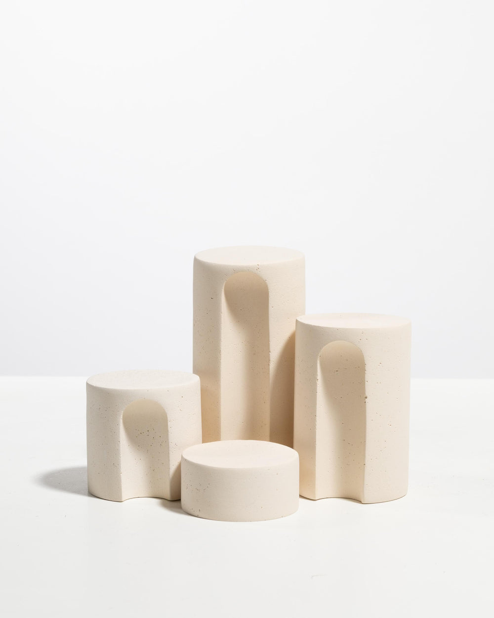 Four off white cylinder podiums with arched cutouts in different heights