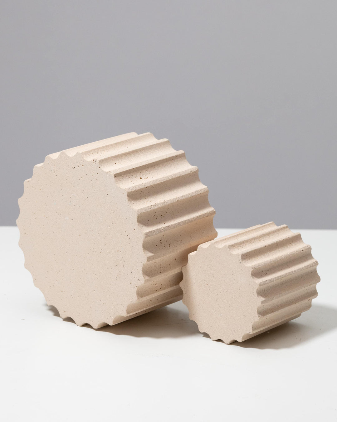 Two fluted cylinder pedestals in speckled beige plaster, different sizes with scalloped edges