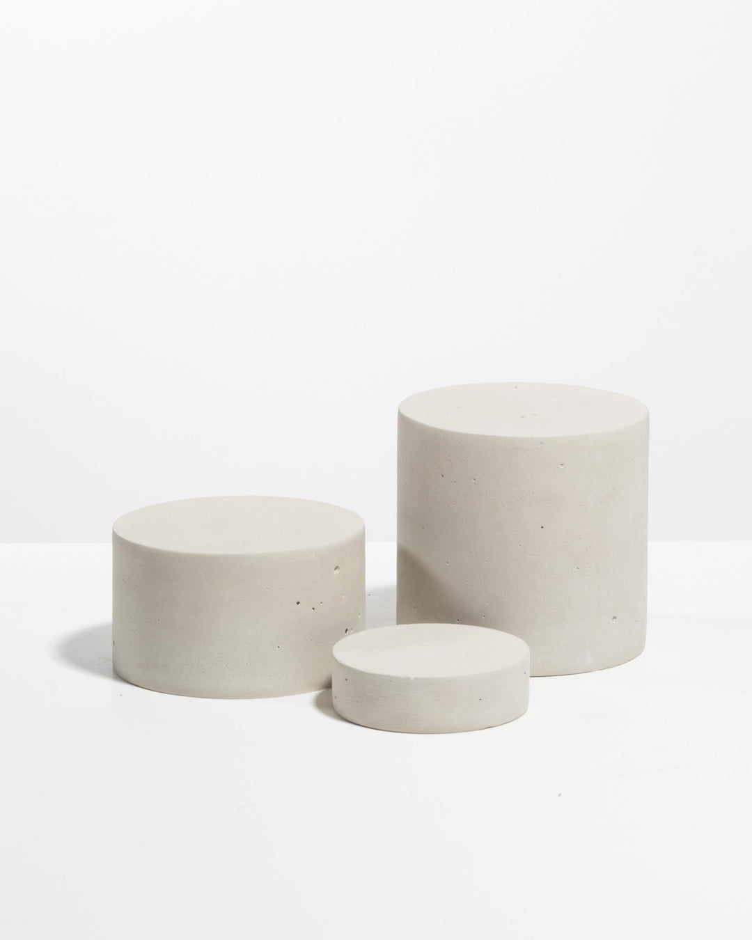 Three light grey plaster cylinder risers of different heights for product display