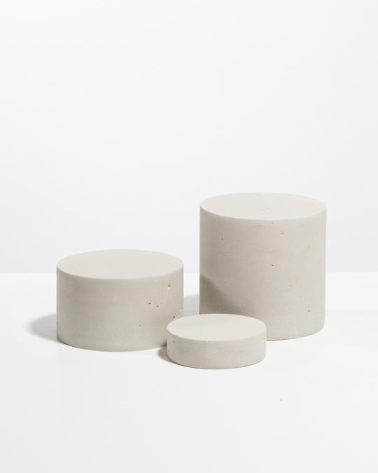 Three light grey plaster cylinder risers of different heights for product display