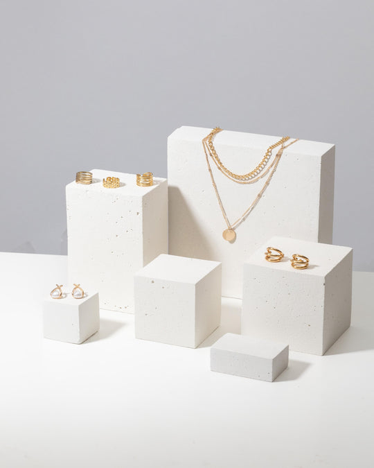 Gold jewelry styled on white textured display blocks
